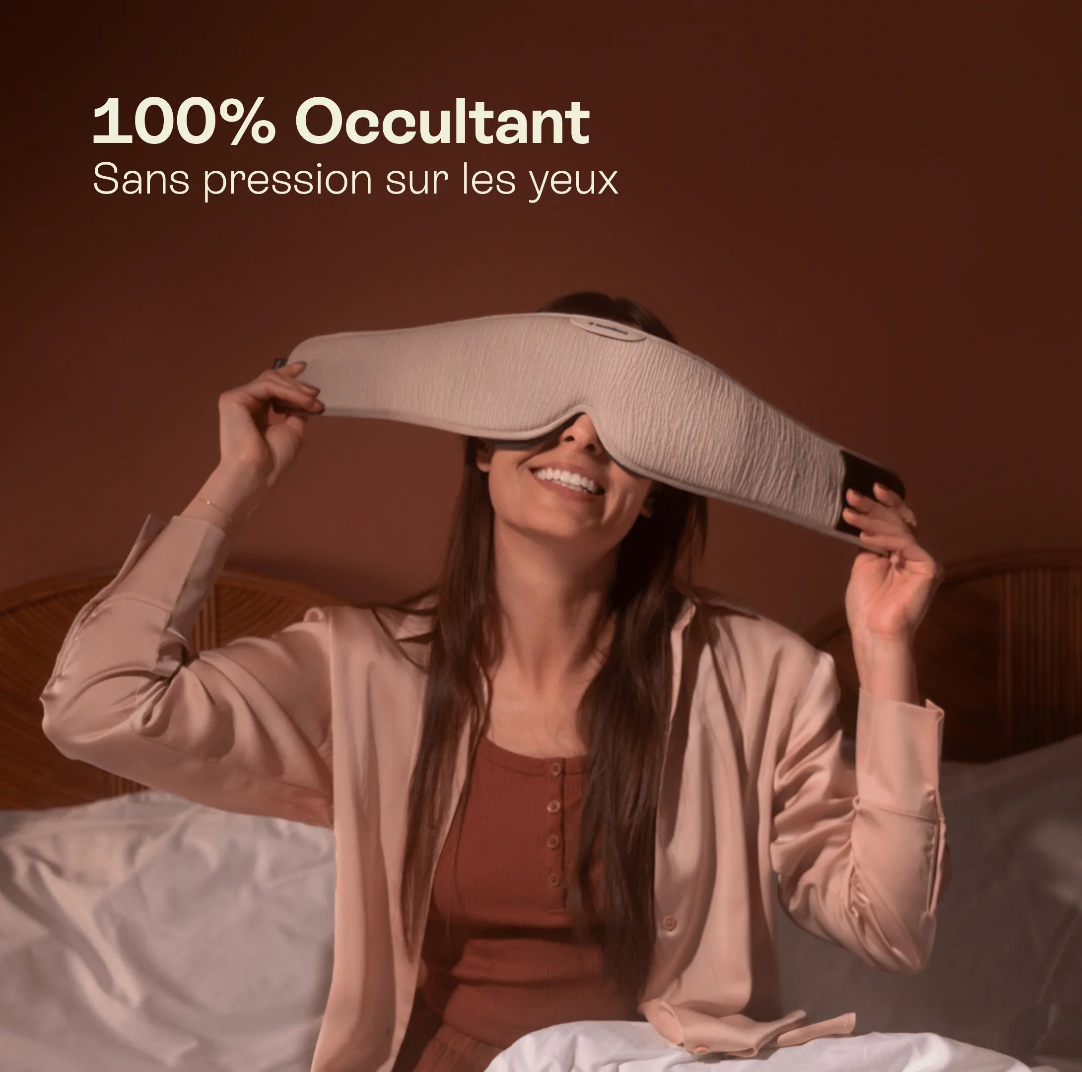 Woman in bed smiling and wearing a large beige blackout sleep mask, text highlights light blocking and no eye pressure.