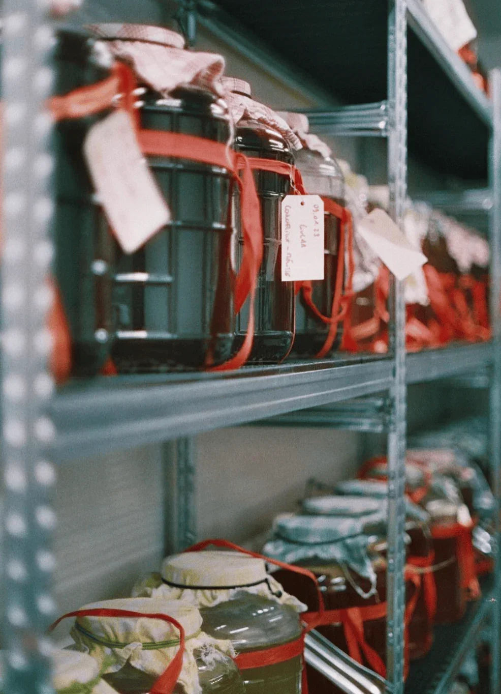 Glass jars with handwritten labels and red ribbons on metal shelving in storage room